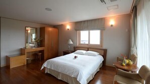 Habitación de hotel con una cama grande, un escritorio con silla, una mesita con frutas y una ventana.