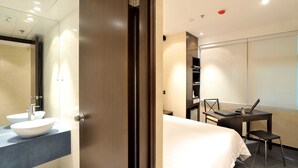 A modern hotel room with a large bed, a desk with a laptop, a chair, and a bathroom with a sink and mirror. - Mingle Place With The Star (Hong Kong)