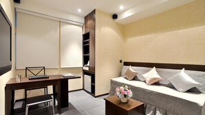 A modern room with a desk, chair, sofa, and a small table with a vase of flowers. - Mingle Place With The Star (Hong Kong)