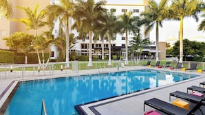 Una piscina con sillones de descanso y palmeras.