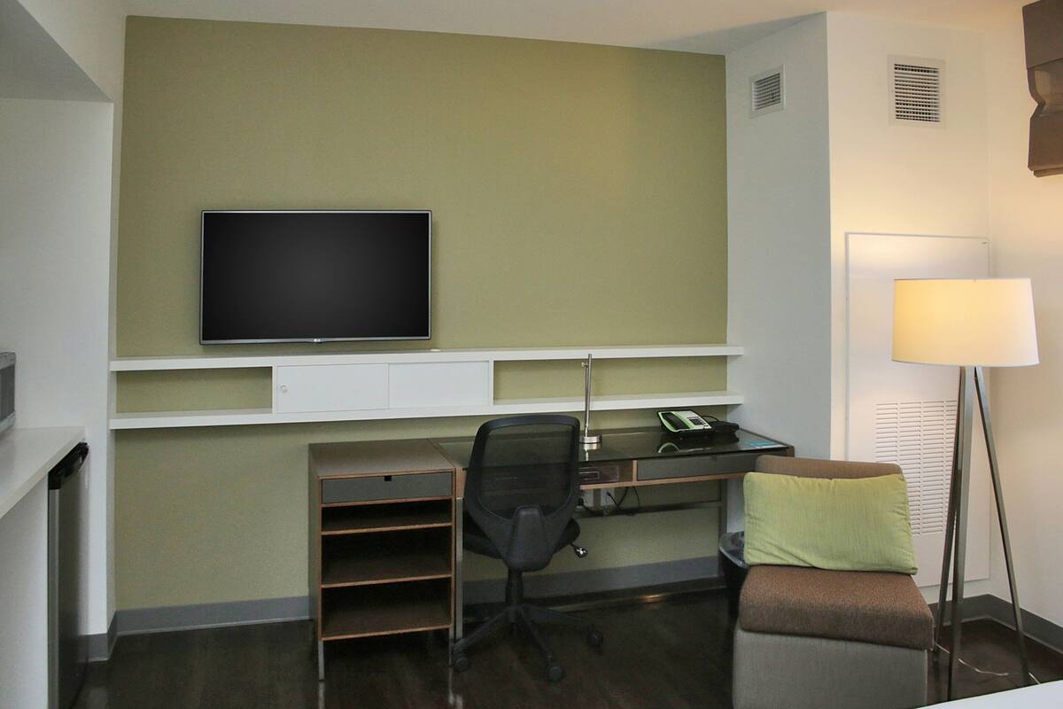 Habitación de hotel con escritorio, silla, televisor, lámpara y una pequeña zona de estar.