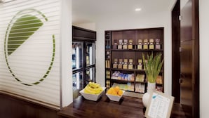 Un área de recepción con un mostrador blanco, un reloj en la pared y un estante con varios objetos, incluyendo una planta y un menú.