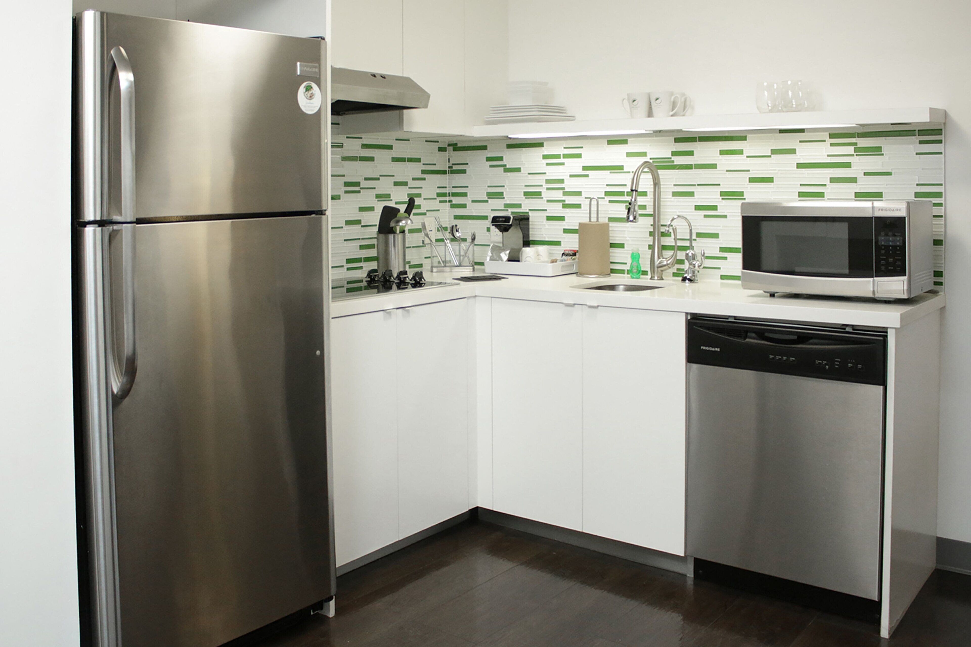 Uma cozinha moderna com eletrodomésticos de aço inoxidável, armários brancos e painel de backsplash verde e branco.