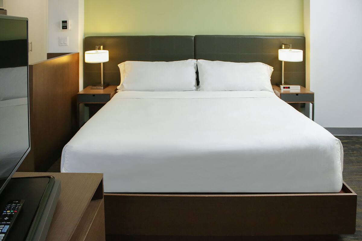 Una cama bien tendida con sábanas blancas, dos lámparas de noche y un cabecero de madera.
