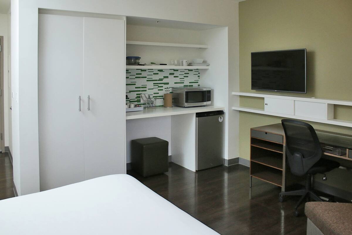 Habitación compacta con cama, escritorio con silla, televisor, microondas y refrigerador pequeño.