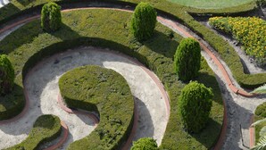 Ein angelegter Garten mit einem gewundenen Pfad, ordentlich geschnittenen Hecken und verschiedenen Sträuchern.