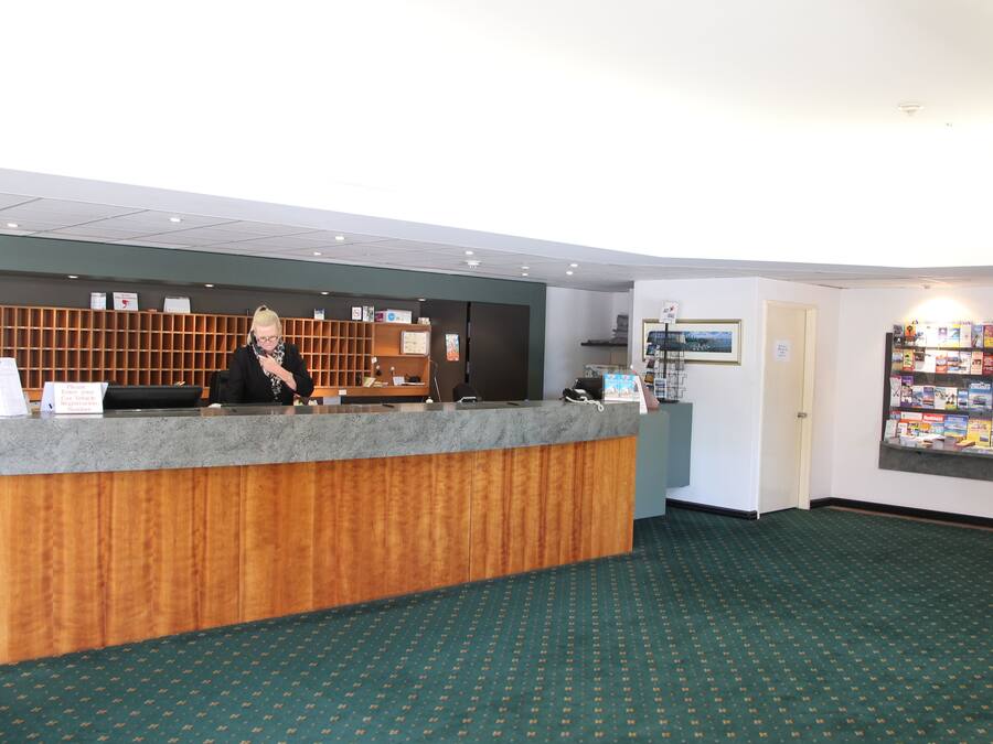 A reception desk with a wooden panel and a grey counter, a wall-mounted information board, and a bulletin board with various items.