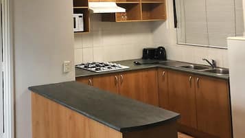 Una cocina con armarios de madera, estufa a gas, microondas y una ventana con persianas.