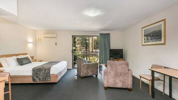 A hotel room with a bed, a desk, a chair, a TV, and a window with a view of trees.