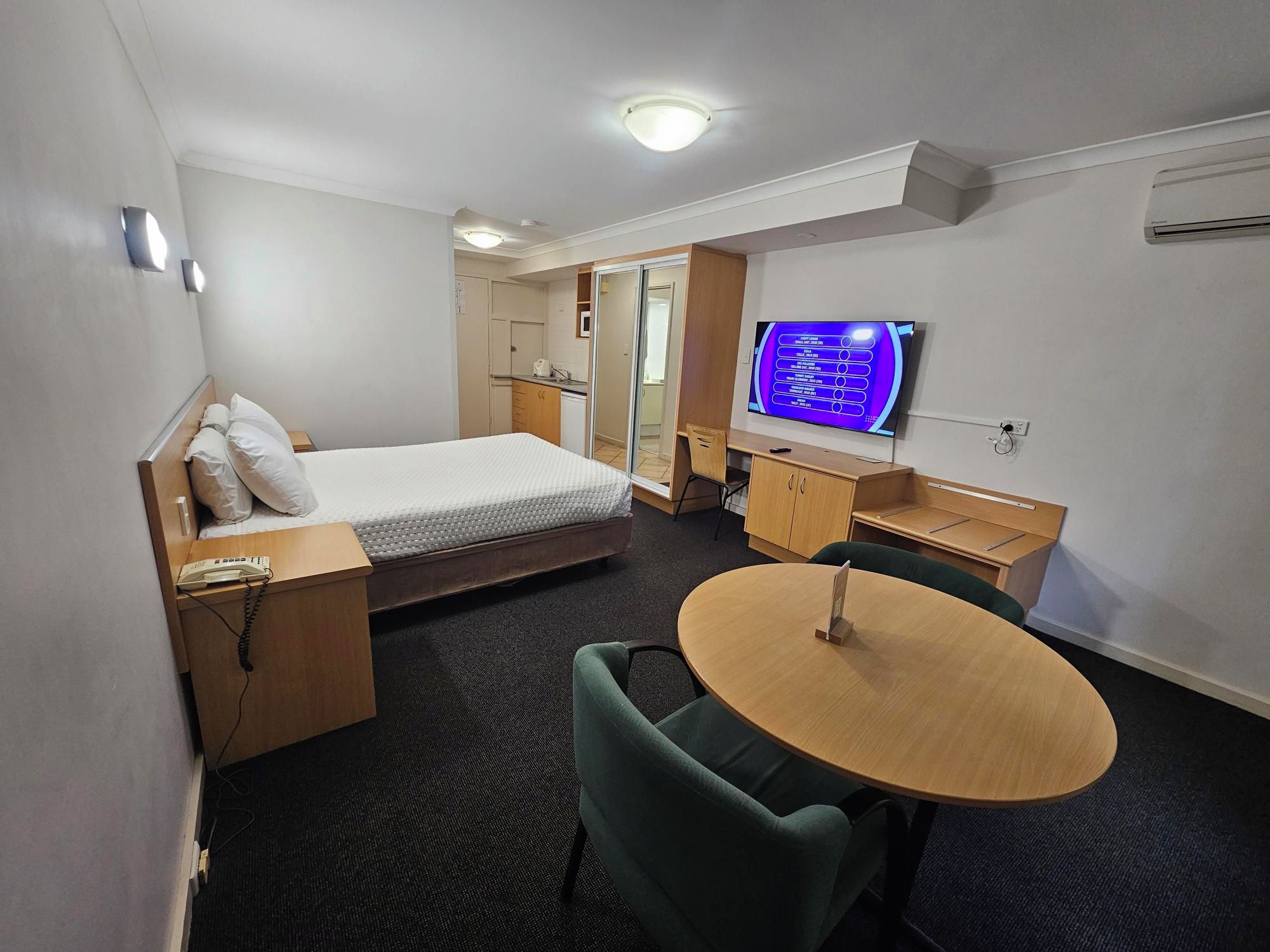 A hotel room with a bed, a desk, a chair, a round table, a television, and a wardrobe.