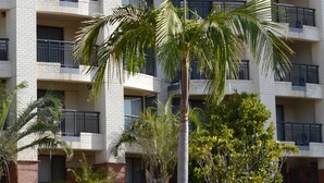 A multi-story hotel with a brick facade, balconies on each floor, and palm trees in the foreground.