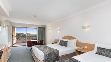 Habitación de hotel con dos camas, un escritorio, una silla y un balcón con vistas.