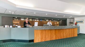 A reception area with a reception desk, a wooden panel, a wall-mounted display, and a patterned carpet.