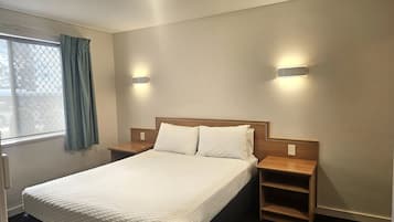 A hotel room with a bed, bedside tables, and wall-mounted lights.