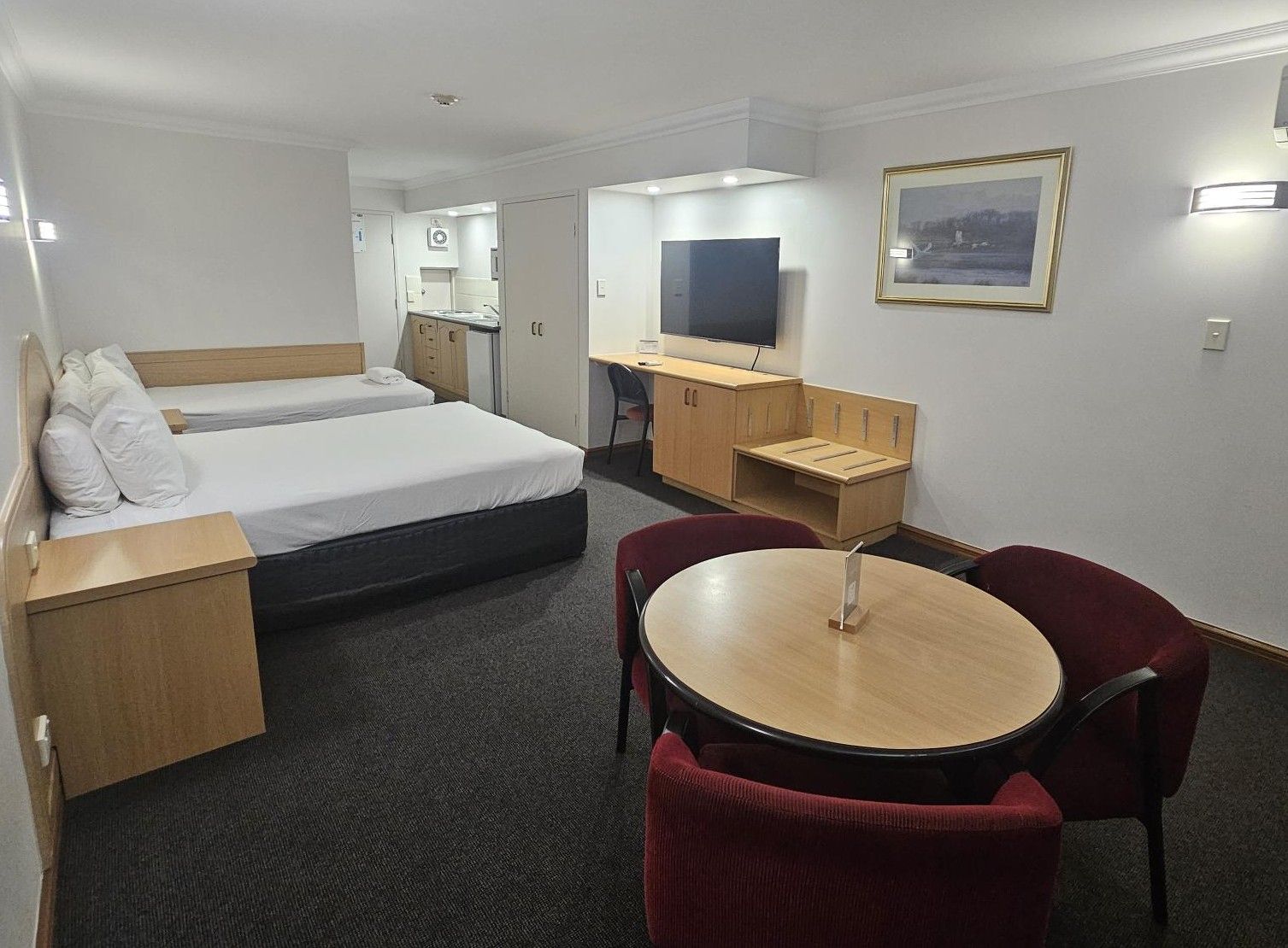 A hotel room with two beds, a desk, a TV, and a dining area with chairs.