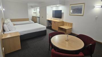 A hotel room with two beds, a desk, a TV, and a dining area with chairs.