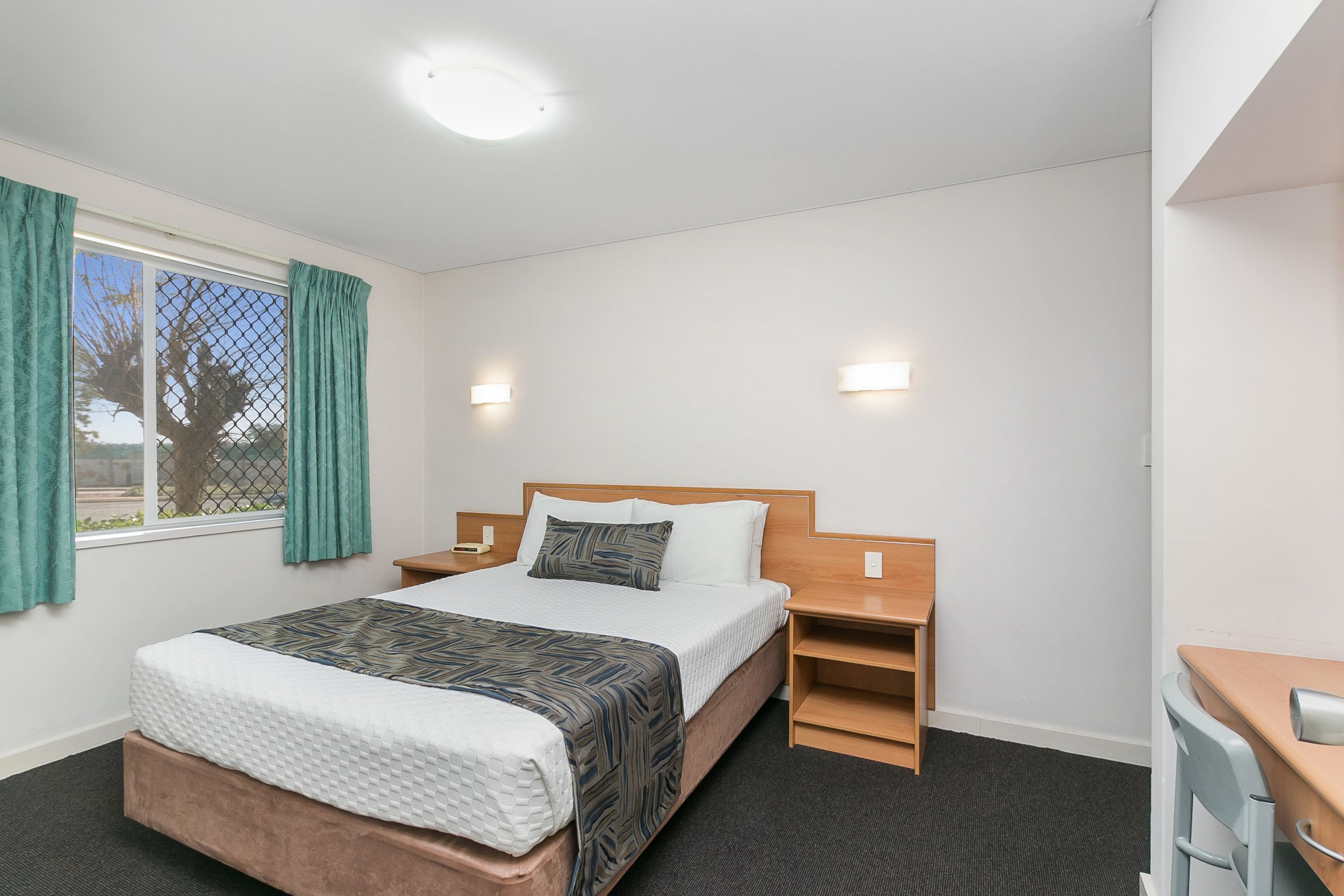 A hotel room with a bed, bedside tables, a desk, and a chair.