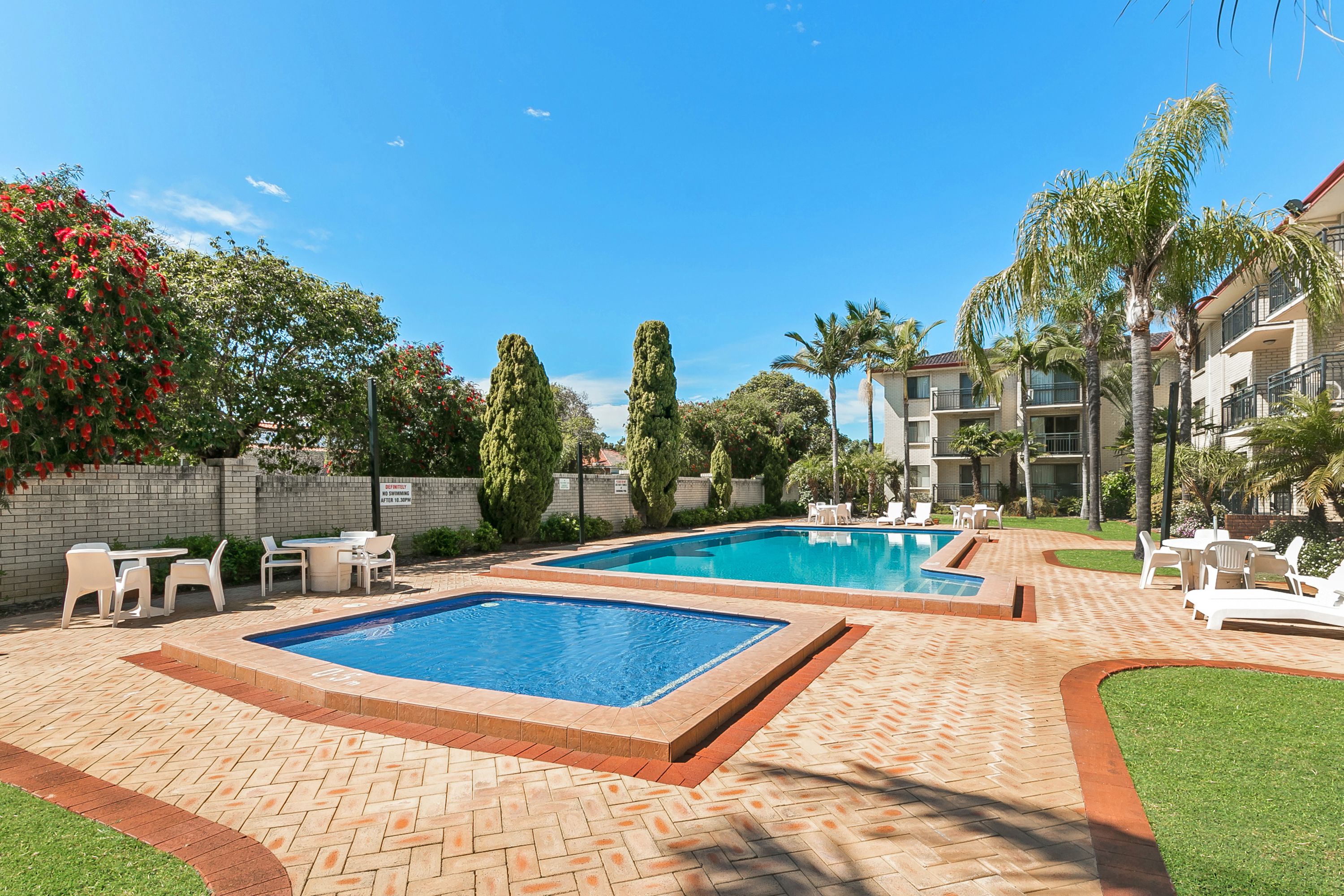 A swimming pool area with two pools, surrounded by lounge chairs and a brick patio.