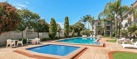 A swimming pool area with two pools, surrounded by lounge chairs and a brick patio.