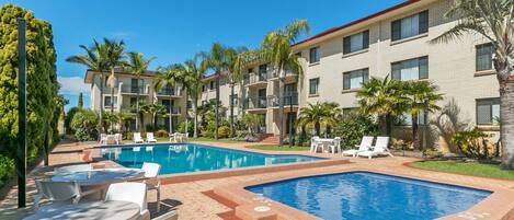 A hotel with a swimming pool, outdoor seating, and palm trees.