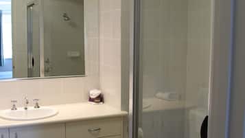 Un baño moderno con ducha envuelta en vidrio, lavamanos blanco y un inodoro.