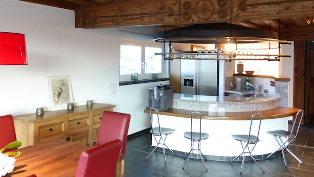 A modern kitchen with a central island, bar stools, and a dining area with a red chair.