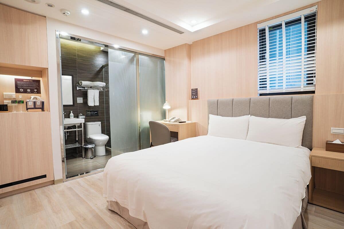 Ein Hotelzimmer mit Bett, Nachttisch, Schreibtisch mit Stuhl, Dusche und Toilette.