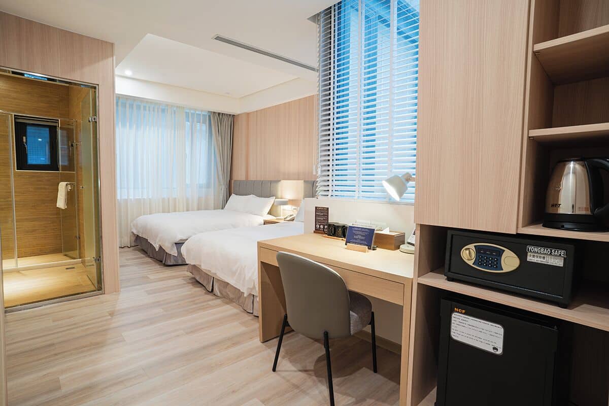 Ein Hotelzimmer mit Bett, Schreibtisch, Stuhl, Minibar und einer Duschkabine.