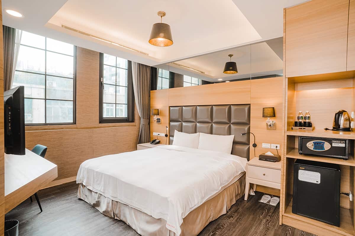 Ein Hotelzimmer mit einem großen Bett, Nachttischen, einem Schreibtisch, einem Fernseher und einer Minibar.