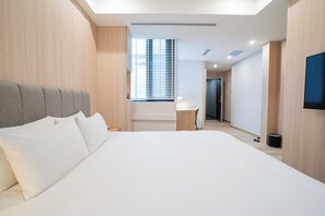 A modern hotel room with a large bed, a desk, and a TV mounted on the wall.
