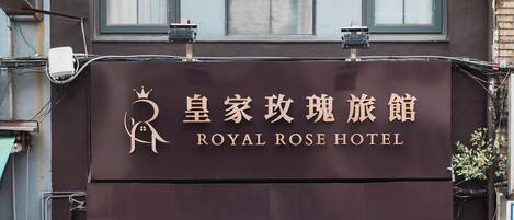 The exterior of the Royal Rose Hotel with a signboard displaying its name in both English and another language.
