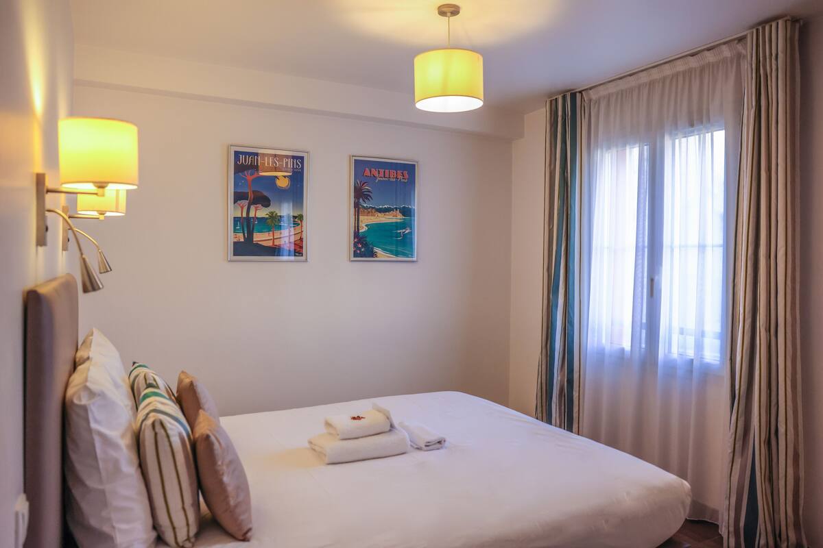 A hotel room with a bed, two wall-mounted lamps, and two framed posters.