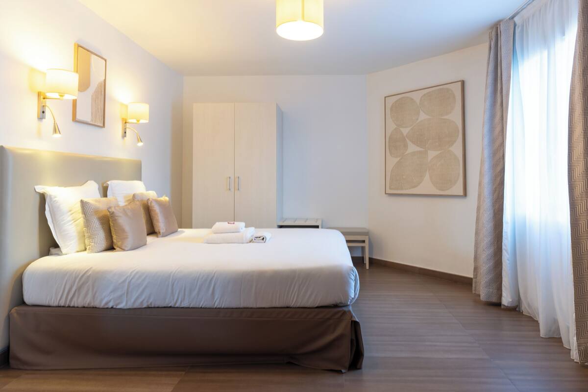 A hotel room with a large bed, bedside lamps, a wardrobe, and a painting on the wall.