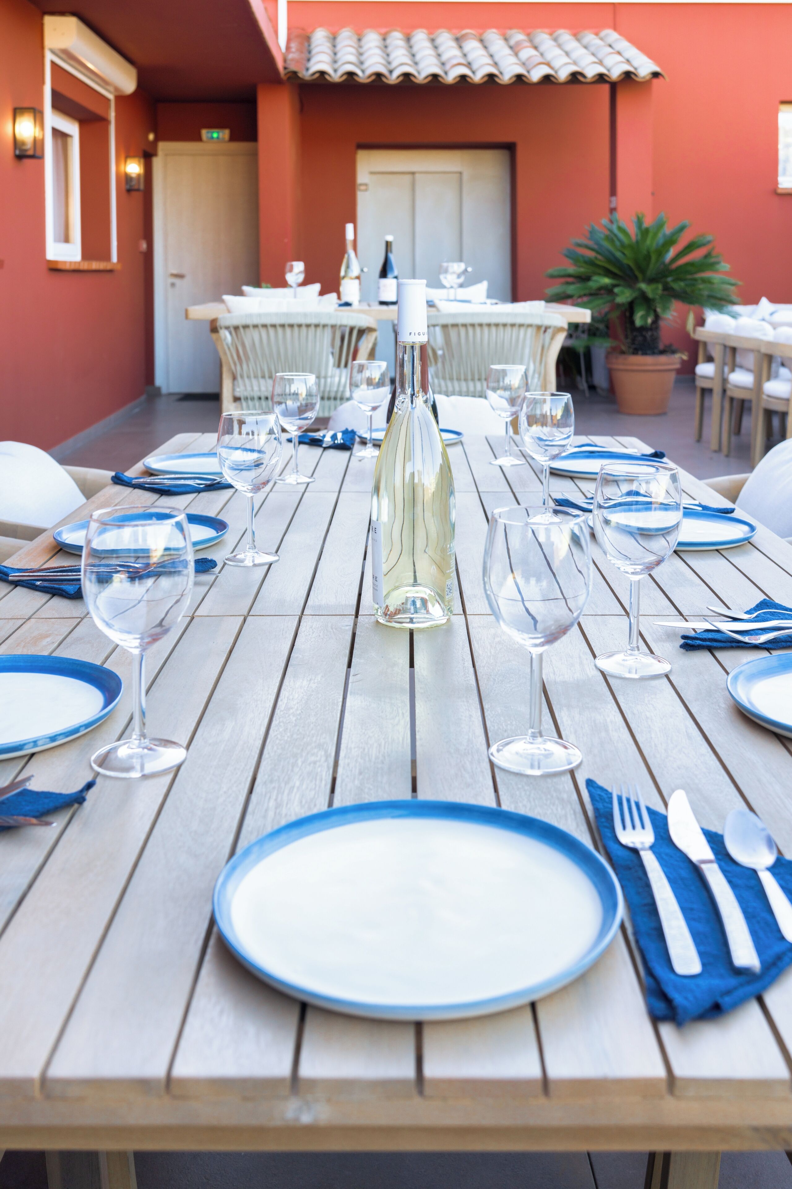 Una mesa de comedor dispuesta con platos azules y blancos, copas de vino y una botella de vino blanco.