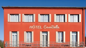 Um edifício vermelho com a placa 'HOTEL CasaBella' e várias janelas com persianas brancas.