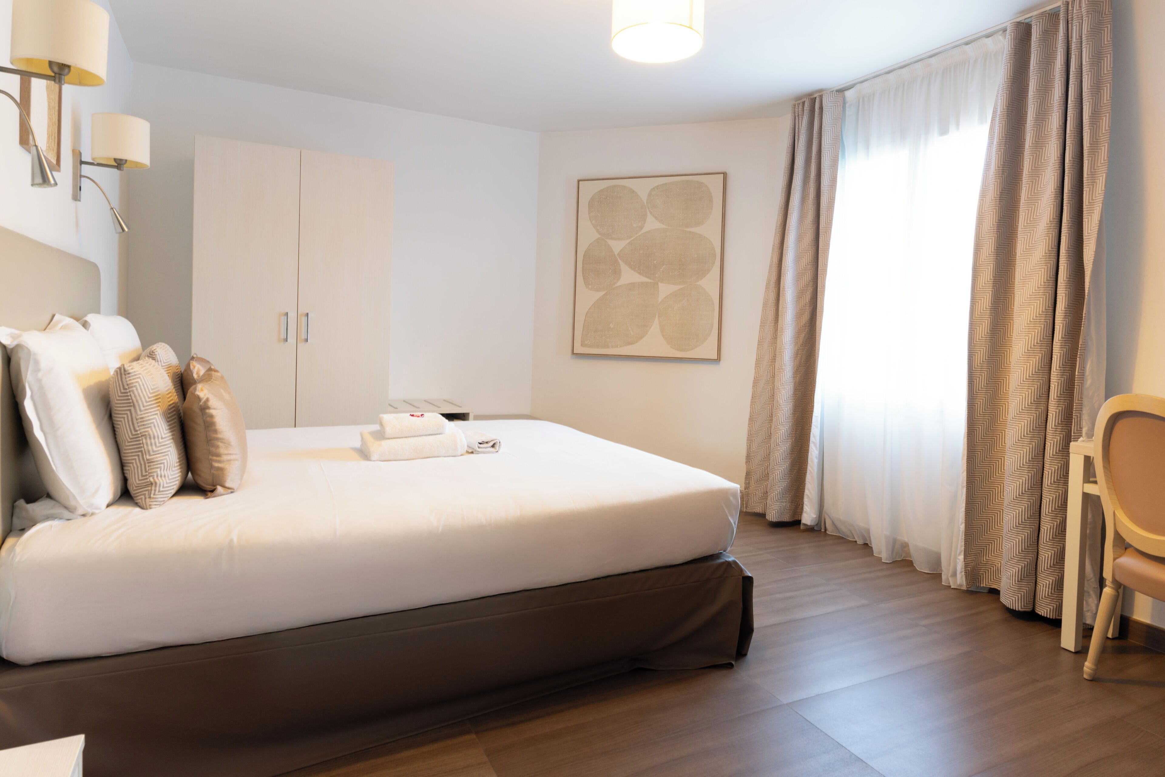 A hotel room with a large bed, a wardrobe, a desk, and a chair.
