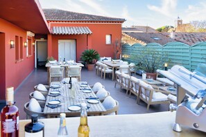 Un área de comedor al aire libre con mesas, sillas, una parrilla y plantas en macetas.