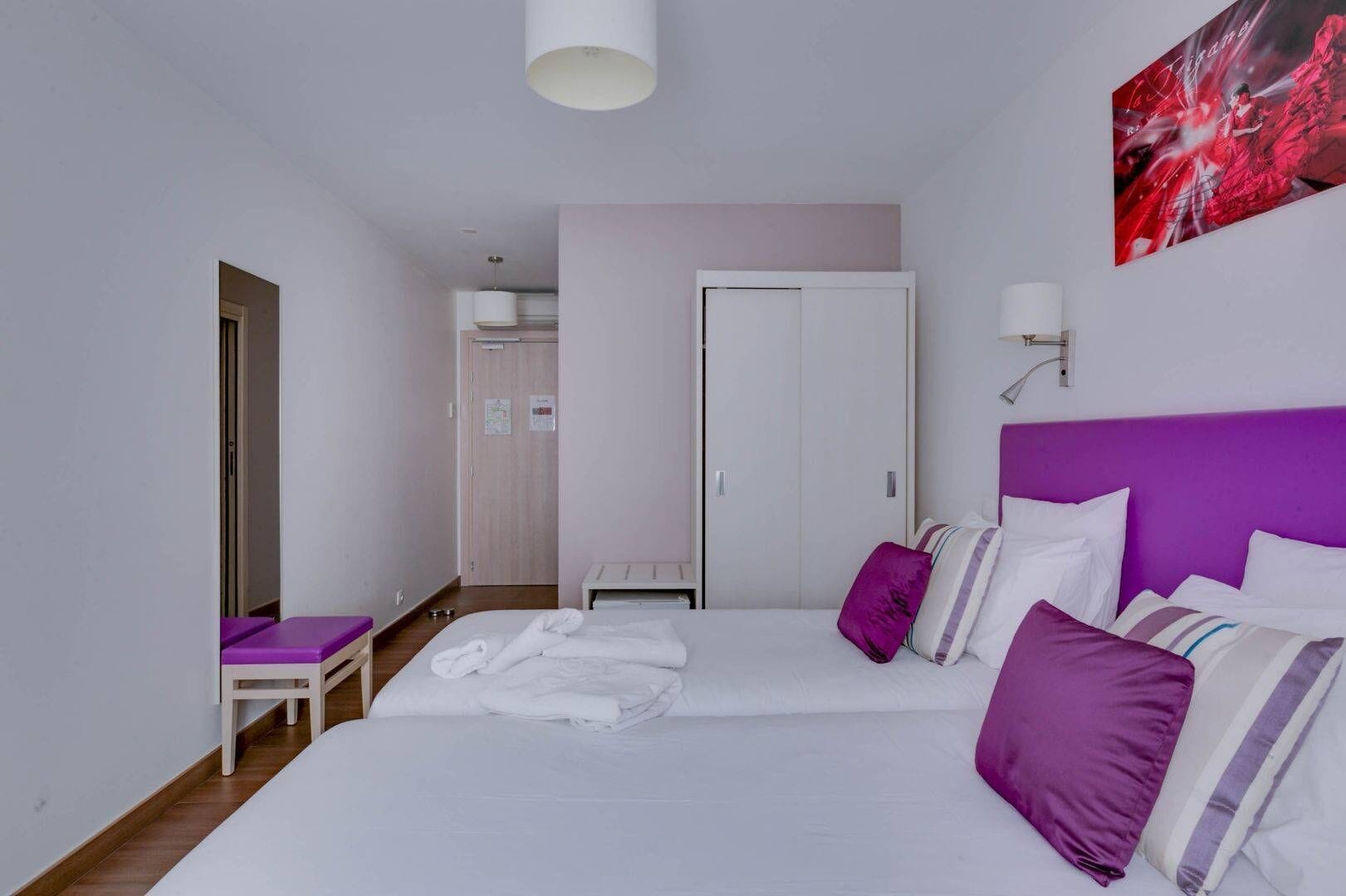 A hotel room with a bed, a small seating area, and a door leading to another room.