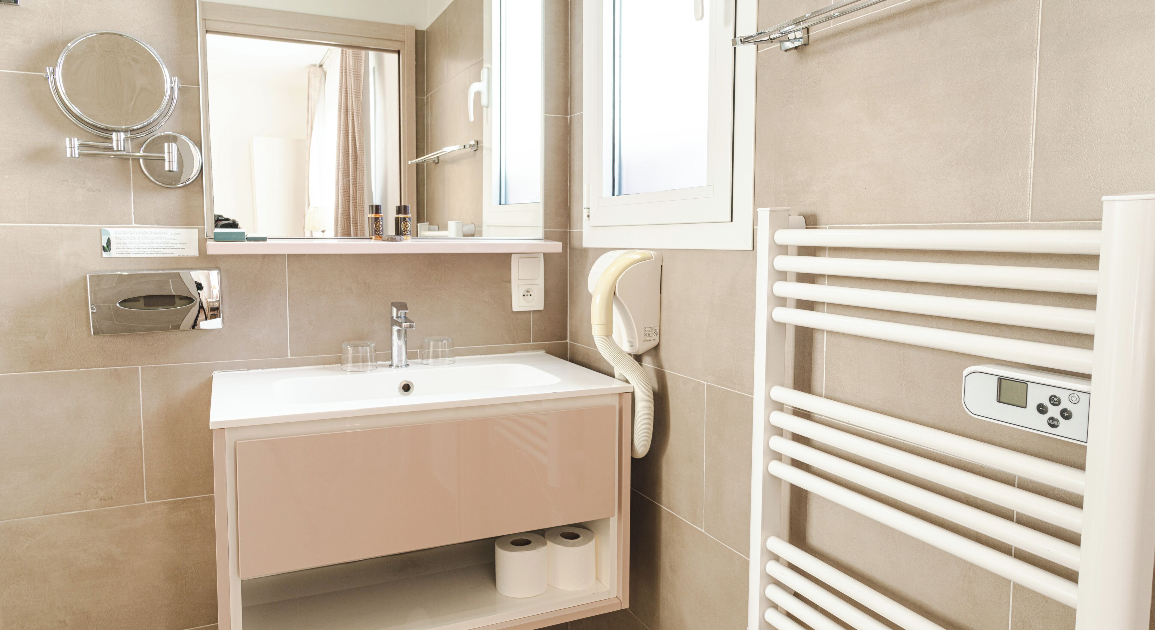 A modern bathroom with a sink, mirror, towel rack, and toilet paper.