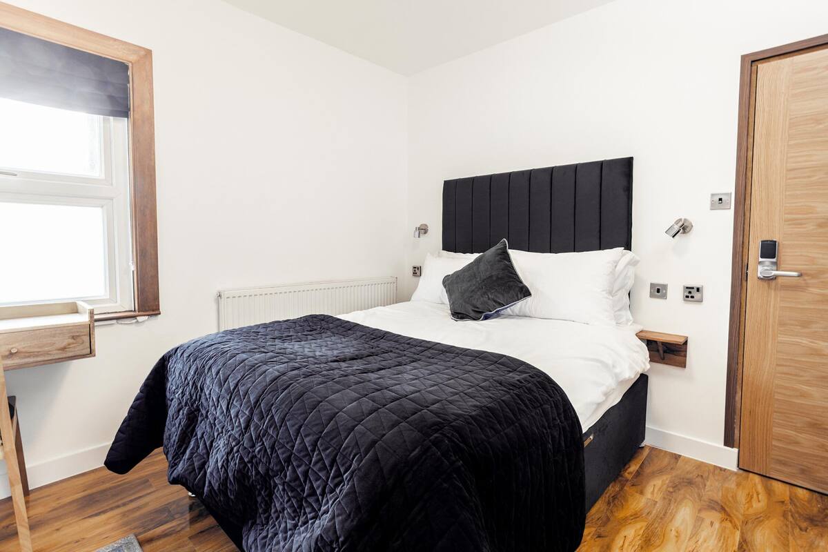 A bedroom with a bed, a nightstand, a wooden door, and a window.