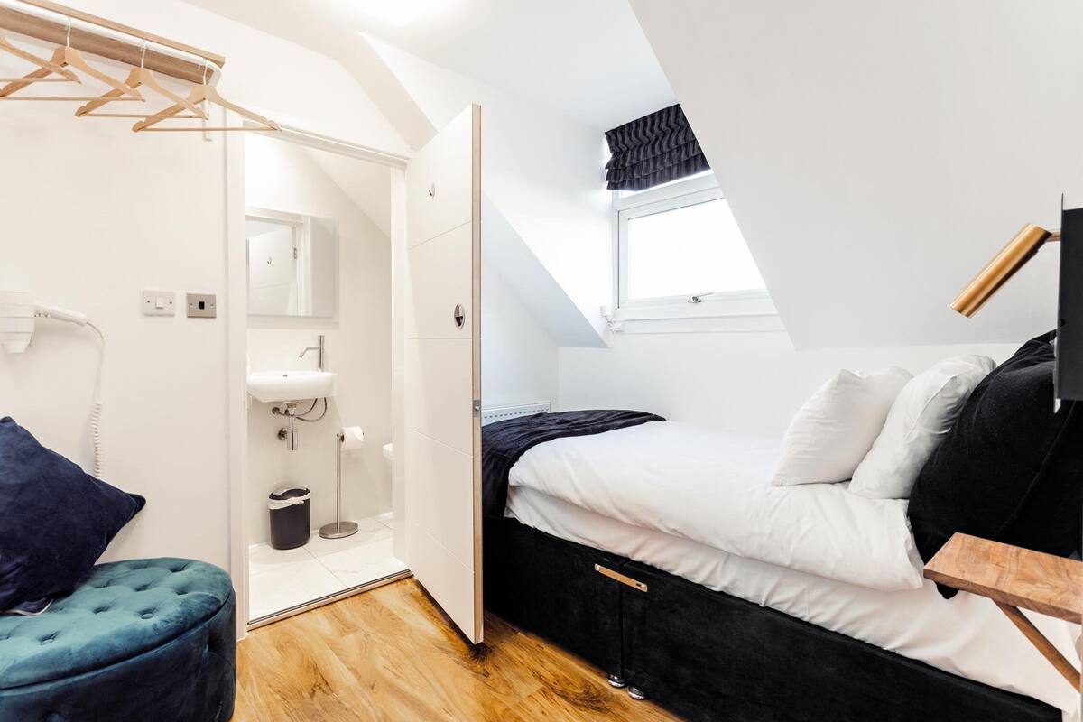 A bedroom with a bed, a bedside table, a hanging light fixture, a window, and a wardrobe.