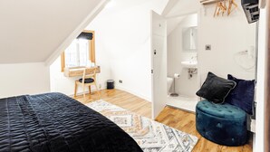 Ett sovrum med en säng, en rund pall, en duschdraperi som hänger upp och ett fönster med utsikt över omgivningen.