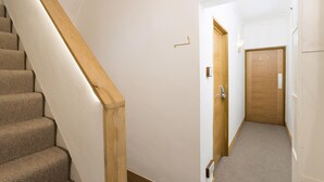En smal hall med en trappa klädd med matta och en trädörr längst ner.