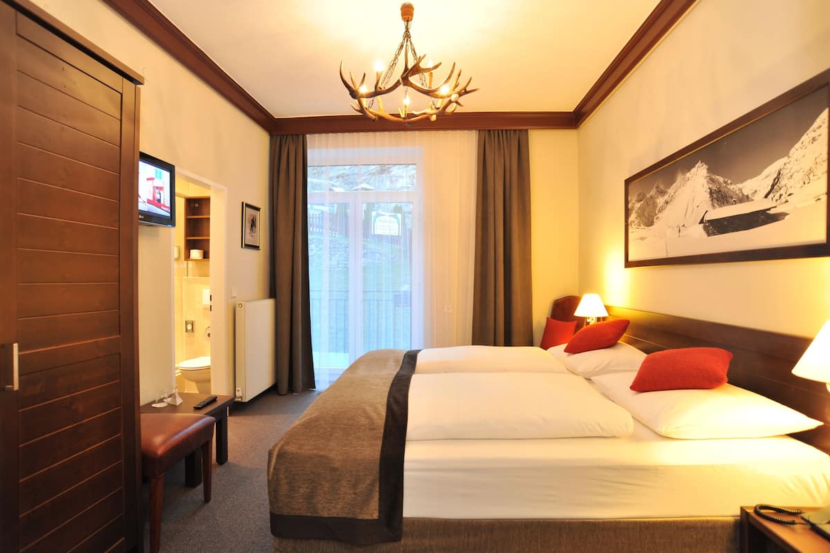 A hotel room with a large bed, two bedside lamps, a television, a desk, and a view of the outdoors.