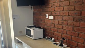 Eine kompakte Küchenzeile mit Mikrowelle, Toaster und einem Flachbildfernseher, der an einer Ziegelwand befestigt ist.