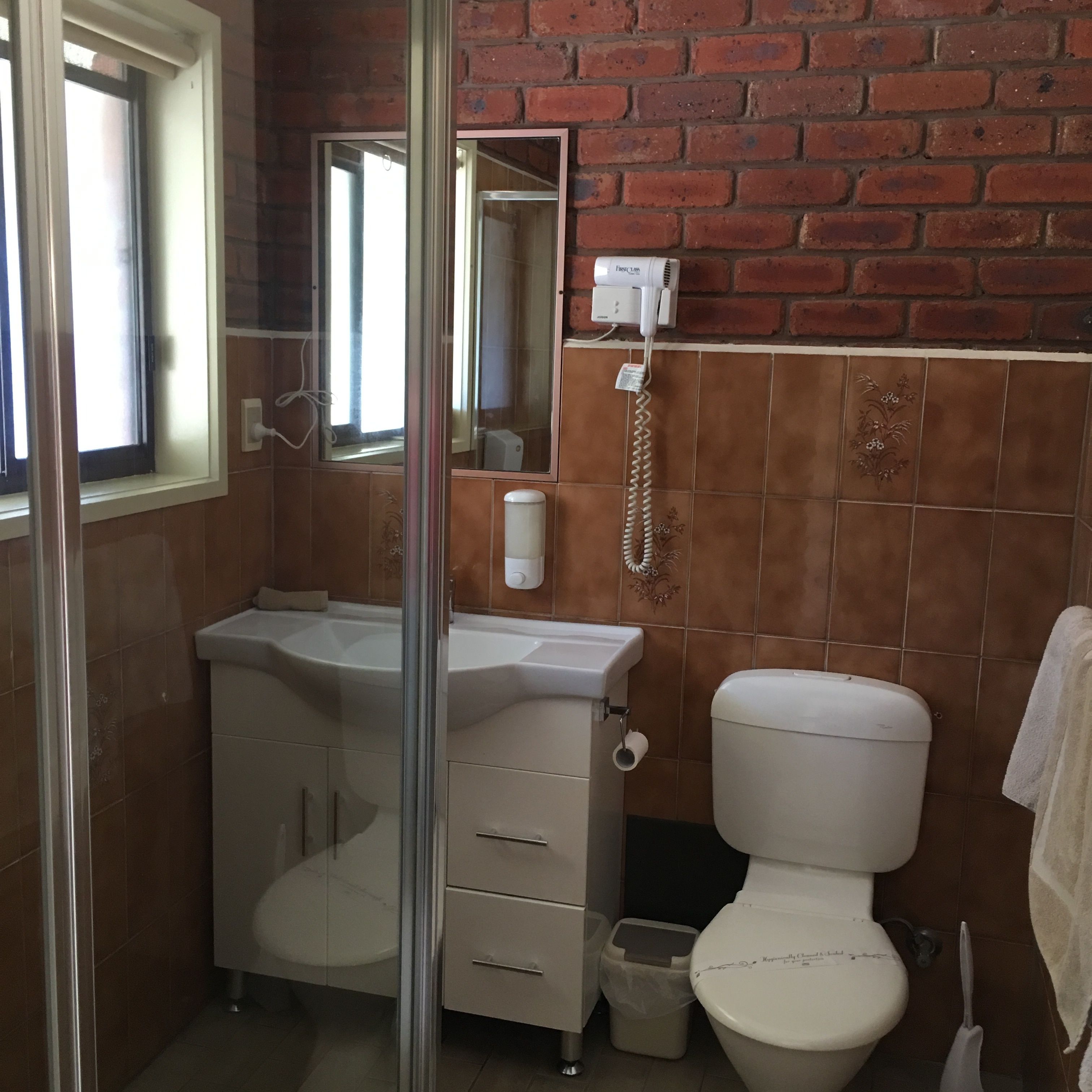 A bathroom with a white sink, a toilet, and a shower. There is a mirror above the sink and a telephone mounted on the wall.