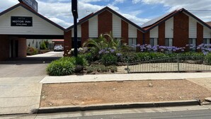 Ein Motel mit deutlicher Beschilderung, einem Parkplatz und einem angelegten Garten mit violetten Blumen.