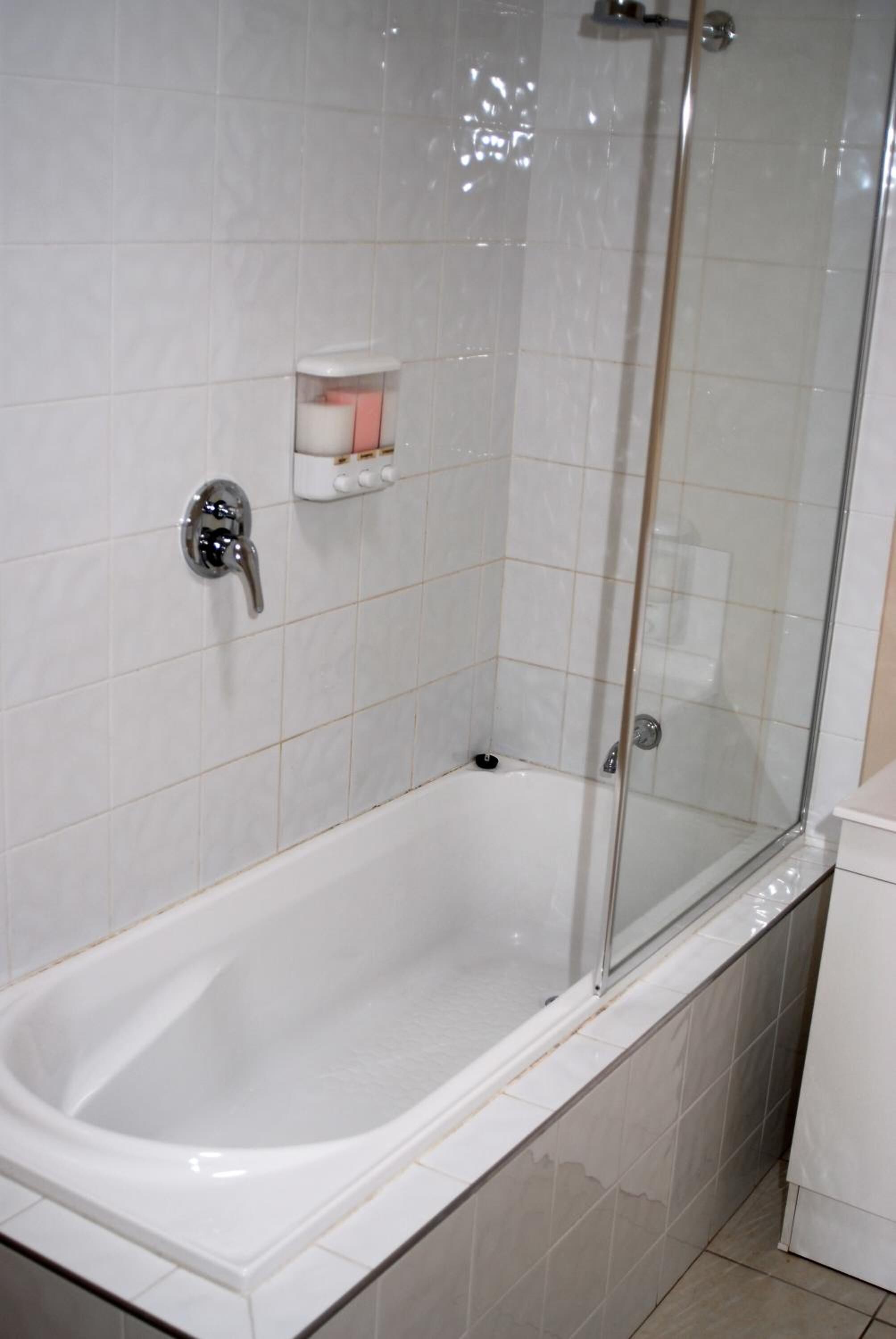 Un baño moderno con ducha de mampara de vidrio, bañera blanca y un estante con artículos de aseo.