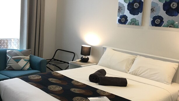 Ein Hotelzimmer mit einem Bett, einem Sessel, einem Nachttisch mit Lampe und zwei an der Wand befestigten Blumenbildern.