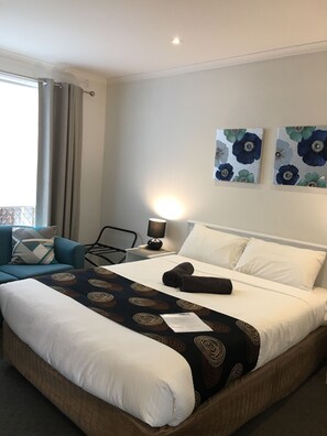 A hotel room with a bed, a chair, a nightstand with a lamp, and two wall-mounted flower paintings.
